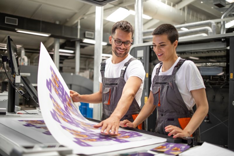 Two prepress workers checking the print quality of a piece in a print shop.