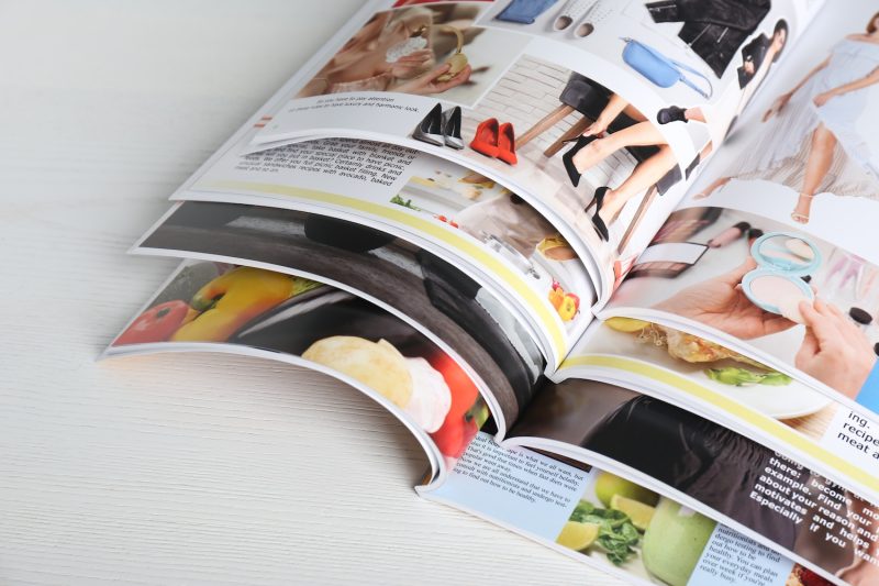 Many open magazines on white wooden table, above view.